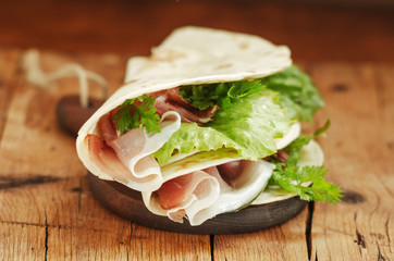 Italian flatbread called piadina with letucce salad, prosciutto crudo on wooden board.