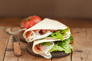Italian flatbread called piadina with letucce salad, prosciutto crudo on wooden board.