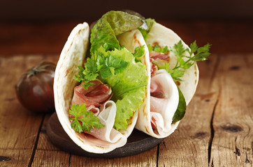 Italian flatbread called piadina with letucce salad, prosciutto crudo on wooden board.