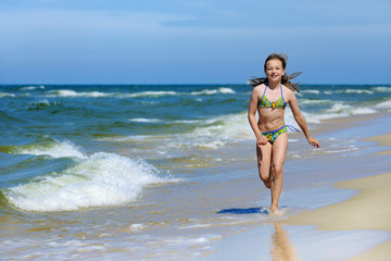 Little girl in swimsuit running on the beach