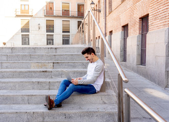 Young handsome man working and studying on laptop in a european city outdoors