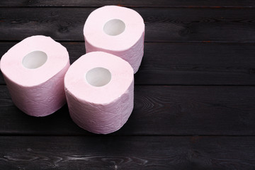 Pastel pink toilet paper rolls on black wooden background