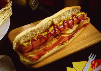Un bocadillo con una barrita de pan, beicon, queso, una salchicha frandkfurt y salsa de mostaza y ketchup.
