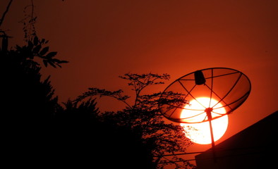 Red hot sun sets behind a satellite dish in Bangkok, Thailand