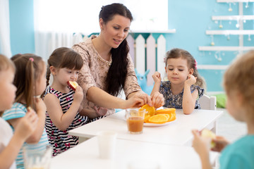 Children and carer together eating fruits in kindergarten or daycare