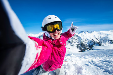 Fototapeta na wymiar Selfie snowboarder. Young happy woman taking selfie with the smartphone on the top of the mountain