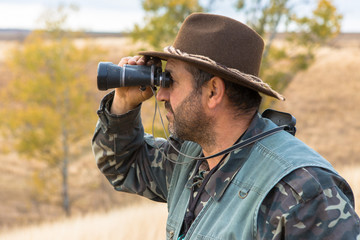 A hunter in a hat with binoculars looks out for prey	