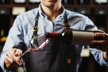 Male sommelier pouring red wine into long-stemmed wineglasses.