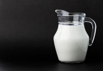 Glass jug of milk on black background with copy space