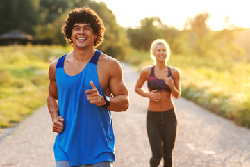 Healthy smiling friends running in nature. Man with curly hair in foreground.