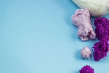 Products for needlework, knitting. Balls of pink, purple yarn on a blue background. Space for text.