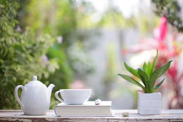 White coffee cup and kettle with notebook on wooden table with green plants