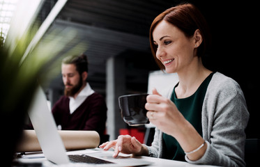A young businesswoman with a cup of coffee working in office, using laptop.