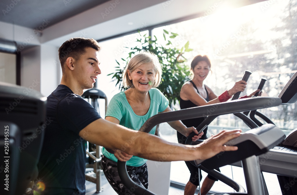 Sticker two cheerful female seniors in gym with a young trainer doing cardio work out.