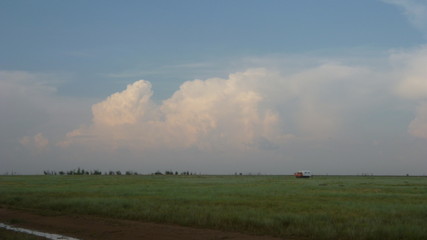 Large cumulonimbus rain clouds creeping over the horizon on a green field with a truck in the middle
