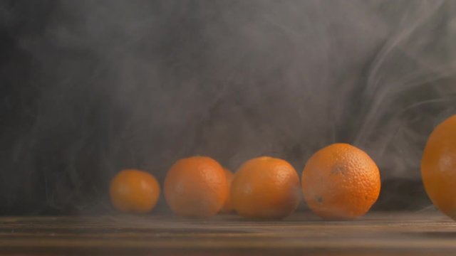 Tangerines roll on a wooden table on a black background in a haze, close-up, slow mo, natural, mandarine