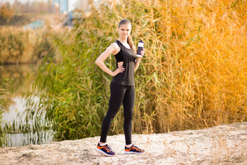 Beautiful fitness athlete woman drinking water after work out exercising on autumn park