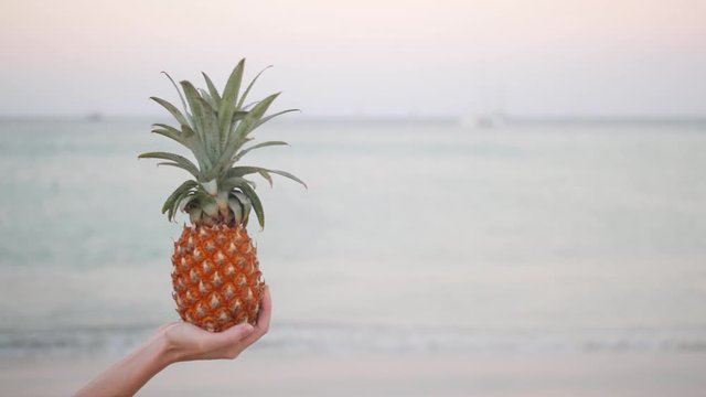 Close up of woman hand holding pineapple cocktail on beach.