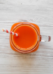 Fresh carrot juice in glass jar on white wooden table, top view. Flat lay, overhead, from above.