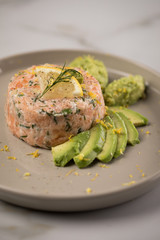 Rohes Lachstatar mit Lachs, Dill, Zitrone, Avocado und Vollkorn Toast Brot auf Porzellan Teller und Marmor Hintergrund