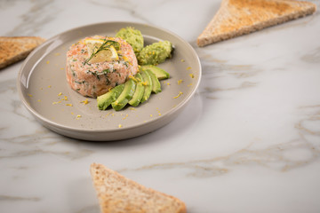 Rohes Lachstatar mit Lachs, Dill, Zitrone, Avocado und Vollkorn Toast Brot auf Porzellan Teller und...