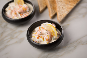 Garnelen Salat mit Lachs Kaviar,  Kräuter, Zitrone, und Vollkorn Toast Brot in schwarzer Schale auf Marmor Hintergrund