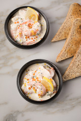 Garnelen Salat mit Lachs Kaviar,  Kräuter, Zitrone, und Vollkorn Toast Brot in schwarzer Schale auf Marmor Hintergrund