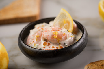 Garnelen Salat mit Lachs Kaviar,  Kräuter, Zitrone, und Vollkorn Toast Brot in schwarzer Schale auf Marmor Hintergrund