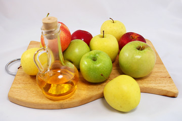 Apples and apple cider vinegar in glass bottle on the wooden board in white background.