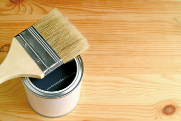 Paintbrush on an opened paint can isolated on wooden background with free space for design or text 