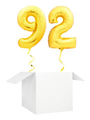 Golden number ninety two inflatable balloon with golden ribbon flying out of blank white box...
