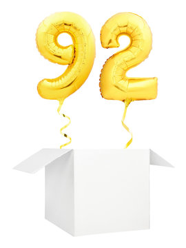 Golden number ninety two inflatable balloon with golden ribbon flying out of blank white box isolated on white background. Birthday concept.