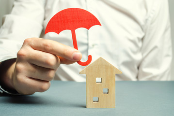 An insurance agent is holding a red umbrella over a wooden house. Property insurance concept....