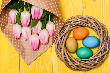 Happy easter season. Easter is coming. Collecting easter eggs. Spring vibes. Colorful eggs and bouquet fresh tulip flowers on yellow background top view. Tradition celebrate easter. Spring holiday
