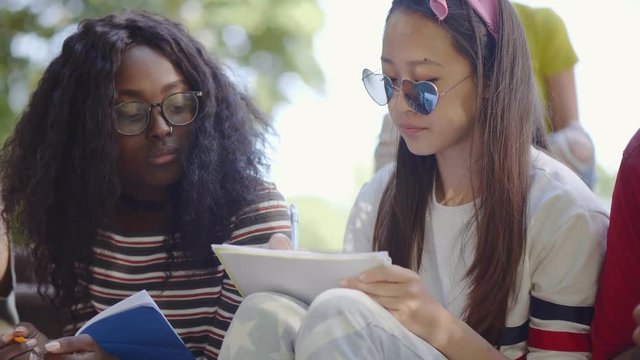 Asian and african girl doing homework sitting outdoors