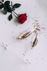 Confetti stars in a glass of champagne, a red rose on a white background, top view