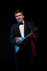 Artist musician, a dark-haired man in a black suit and a bow tie, plays a balalaika in blue and red...
