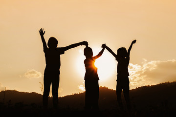 Silhouette group children with raised hands playing on mountain at sunset time.