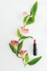 top view of composition with pink flowers, green leaves and lipstick on white background
