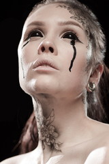 portrait of young brunette girl with black tears from eyes and lace pattern on face and neck posing...
