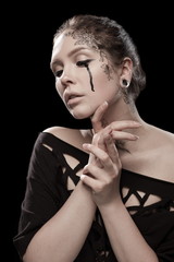 portrait of young brunette girl with black tears from eyes and lace pattern on face and neck posing...
