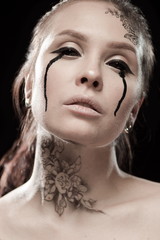 portrait of young brunette girl with black tears from eyes and lace pattern on face and neck posing...