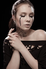 portrait of young brunette girl with black tears from eyes and lace pattern on face and neck posing...