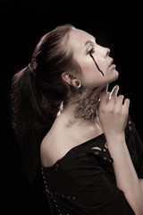 portrait of young brunette girl with black tears from eyes and lace pattern on face and neck posing...