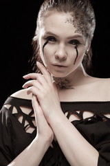 portrait of young brunette girl with black tears from eyes and lace pattern on face and neck posing...