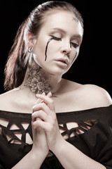 portrait of young brunette girl with black tears from eyes and lace pattern on face and neck posing...