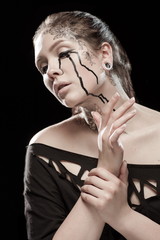 portrait of young brunette girl with black tears from eyes and lace pattern on face and neck posing...