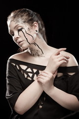 portrait of young brunette girl with black tears from eyes and lace pattern on face and neck posing...