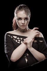 portrait of young brunette girl with black tears from eyes and lace pattern on face and neck posing...
