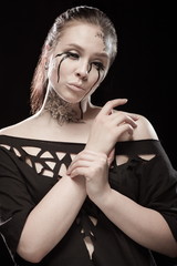 portrait of young brunette girl with black tears from eyes and lace pattern on face and neck posing...